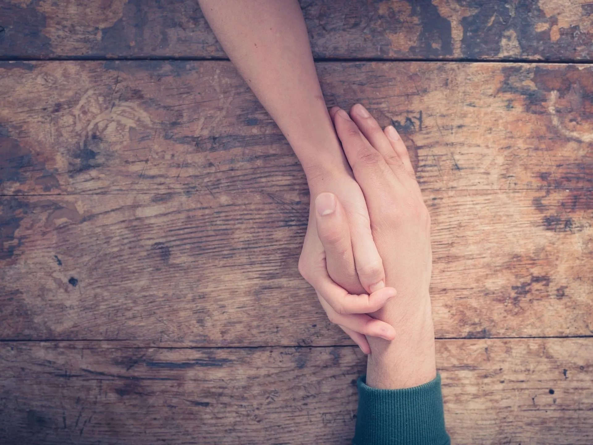 A person holding another persons hand over a wooden table.