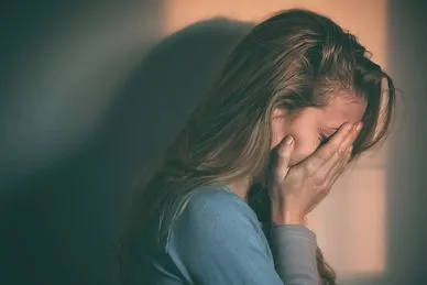 A woman is holding her head in front of the wall.